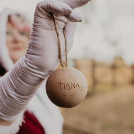 A person holding up a single wooden Christmas bauble with the name 'TIANA' engraved on it.