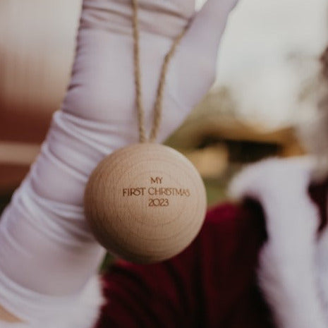 A person holding up a single wooden Christmas bauble with the name 'TIANA' engraved on it.